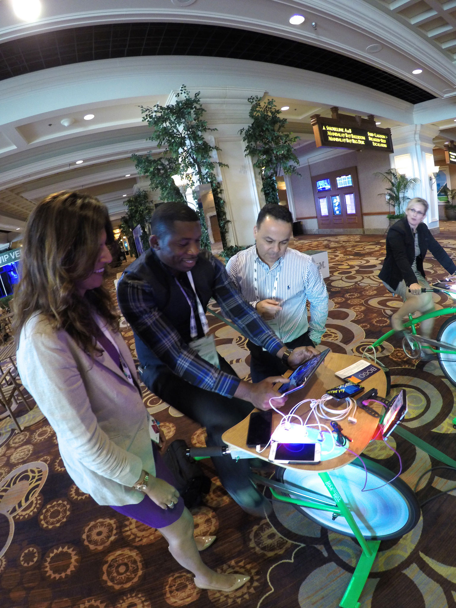 Conference attendees in business attire charging their phones on a green Recharge Station bike